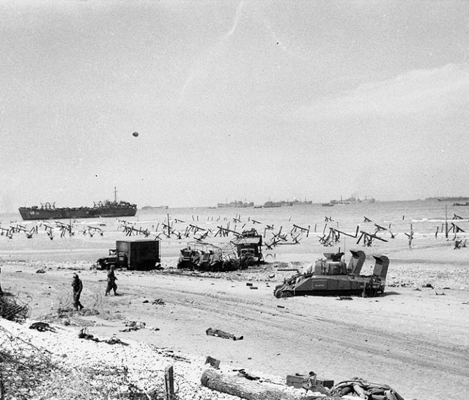 Scene on 'Omaha' beach on the afternoon of 'D-Day', June 6, 1944, showing casualties on the beach, a bogged-down 'Sherman' tank, several wrecked trucks and German anti-landing obstructions