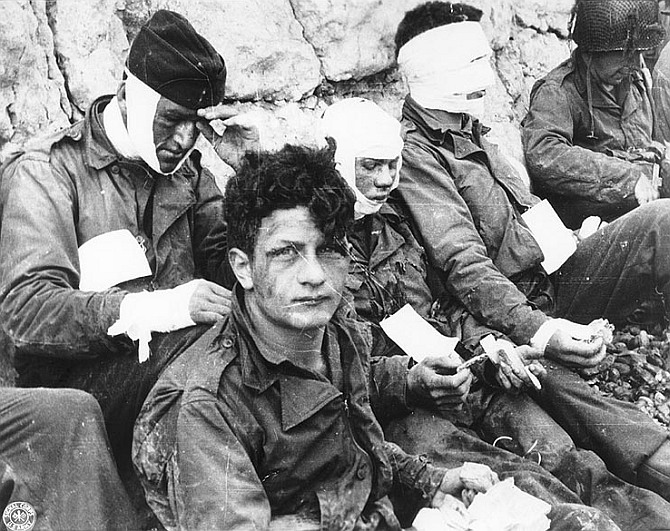 Wounded men of the 3rd Battalion, 16th Infantry Regiment, 1st Infantry Division, receive cigarettes and food after they had stormed 'Omaha' beach