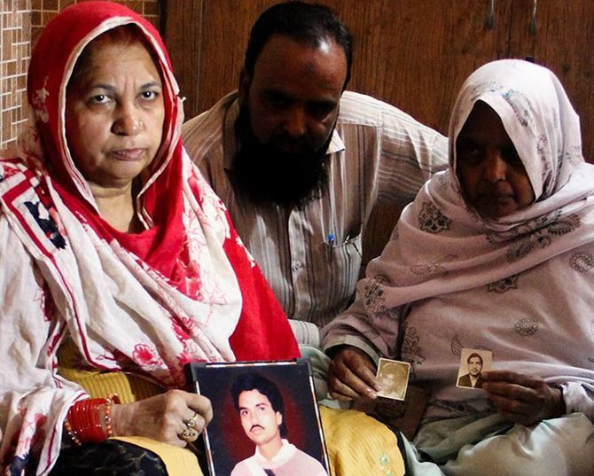 Zulfikar Nasir gives moral support to Shamim Bano, left, who is holding a photograph of her only brother, who was shot by the PAC. Zarina, right, who never speaks, with photographs of her husband and son. Both were killed in 1987. Photograph: Uttam Ghosh/Rediff.com