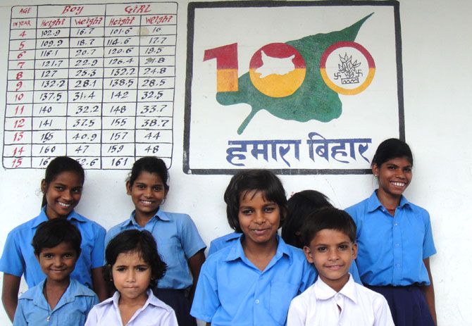 A group of school children pose against a Hamara Bihar mural and details of heights and weights for each child.