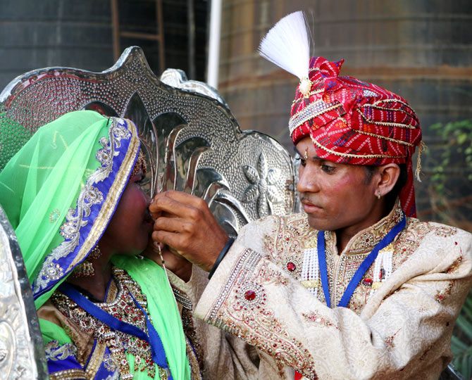 A groom helps his bride fix her nose ring.