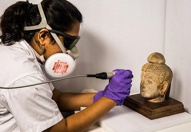 The surface grime is being removed from the head of a Buddha