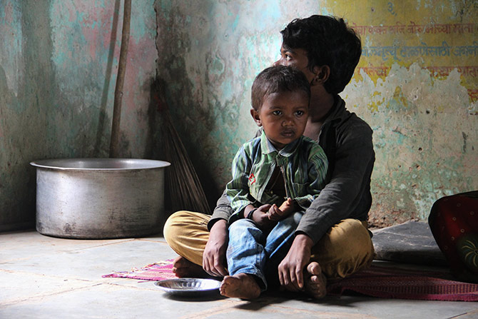 A pensive child awaits the afternoon meal. Till then he decides to sit quietly on his brother's lap.