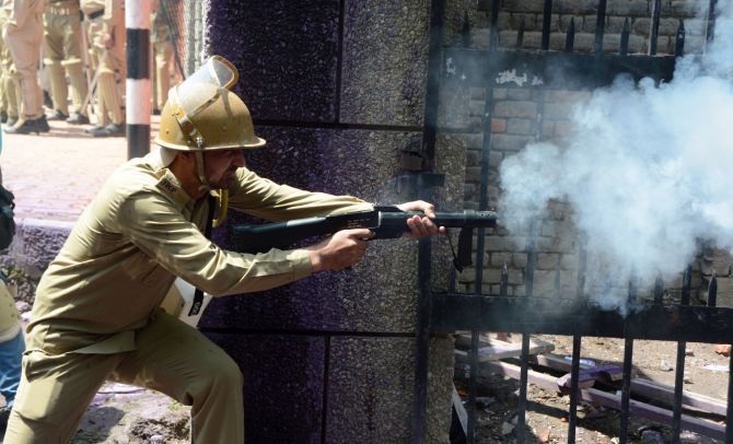 A J&K police personnel fires a tear gas shell