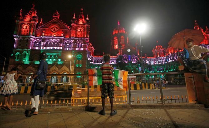 A boy selling flags awaits customers opposite Mumbai's famed Chhatrapati Shivaji Terminus, illuminated in the colours of India's national flag, August 14, 2018. Photograph: Francis Mascarenhas/Reuters