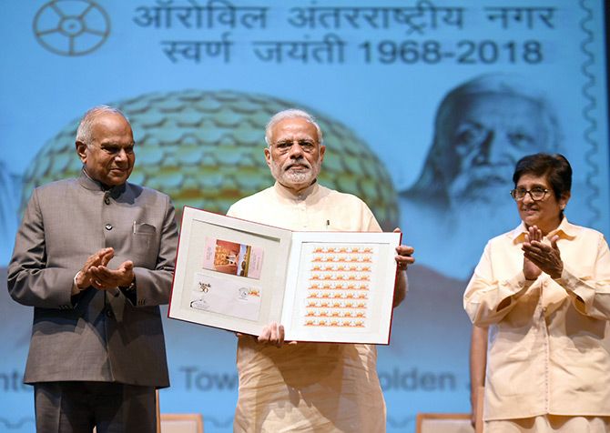 Prime Minister Narendra D Modi, flanked by Tamil Nadu Governor Banwarilal Purohit, left, and Puducherry Lieutenant Governor Kiran Bedi releases a stamp to honour Auroville at Auroville, February 25, 2018. Photograph: Press Information Bureau
