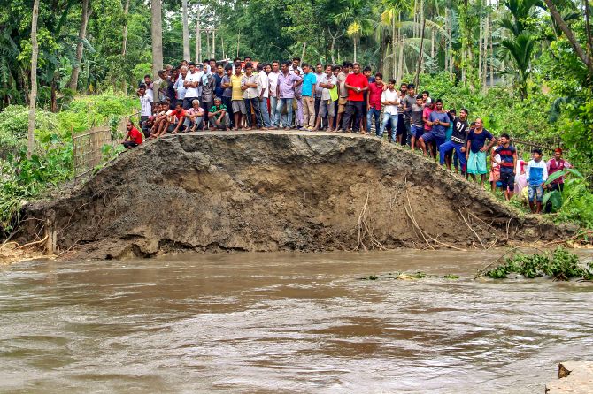 People stand on a damaged embarkment washed out by the floods due to incessant rainfalls, at Hajo in Kamrup