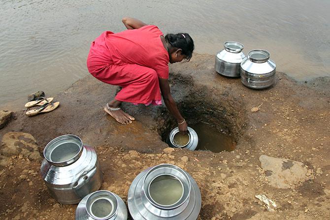 A woman fetches water from an opening made to filter water next to a polluted lake in Thane, outside Mumbai. Photograph: Prashant Waydande/Reuters.