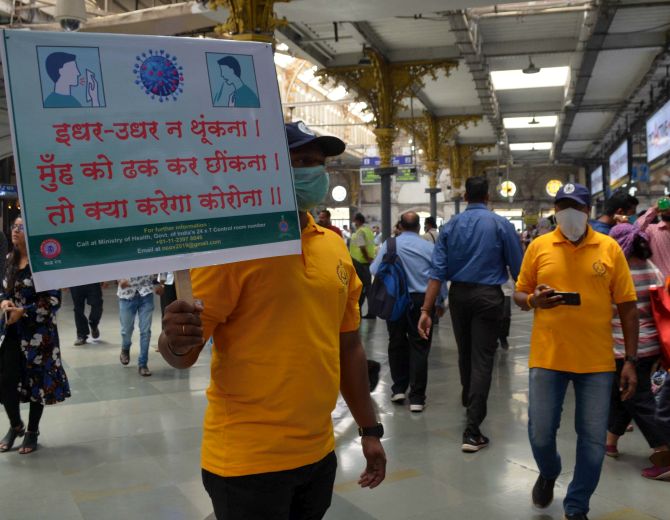 A volunteer holds a placard to create awareness about COVID-19 at the Chhatrapati Shivaji Maharaj Terminus in Mumbai. Photograph: Sahil Salvi