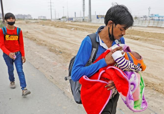 An Indian feeds his newborn baby as he walks on a highway looking out for transport to return to his village