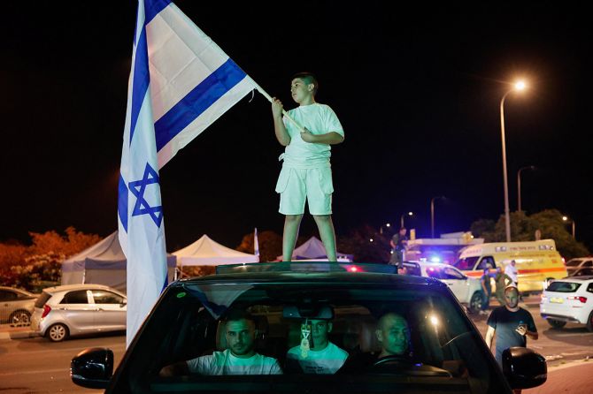 boy holds an Israeli flag while standing on top of a car