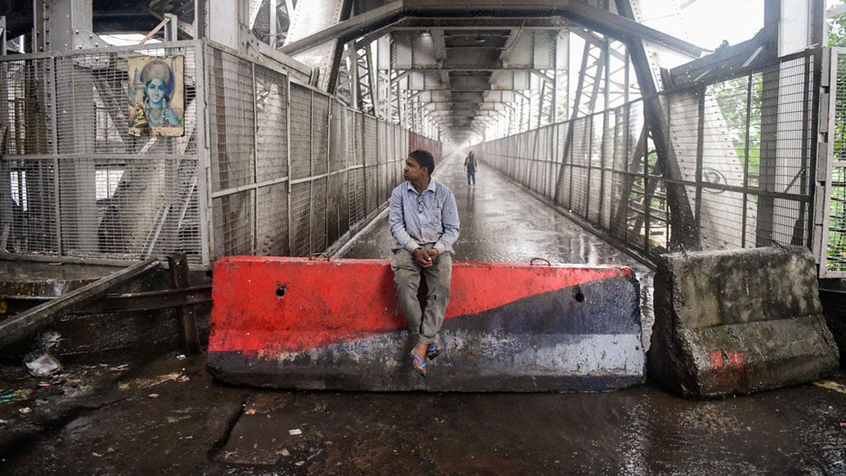 A man sits on a barricade installed to close the entry to the Loha Pul as the river Yamuna crosses the danger mark following incessant rainfall, in New Delhi