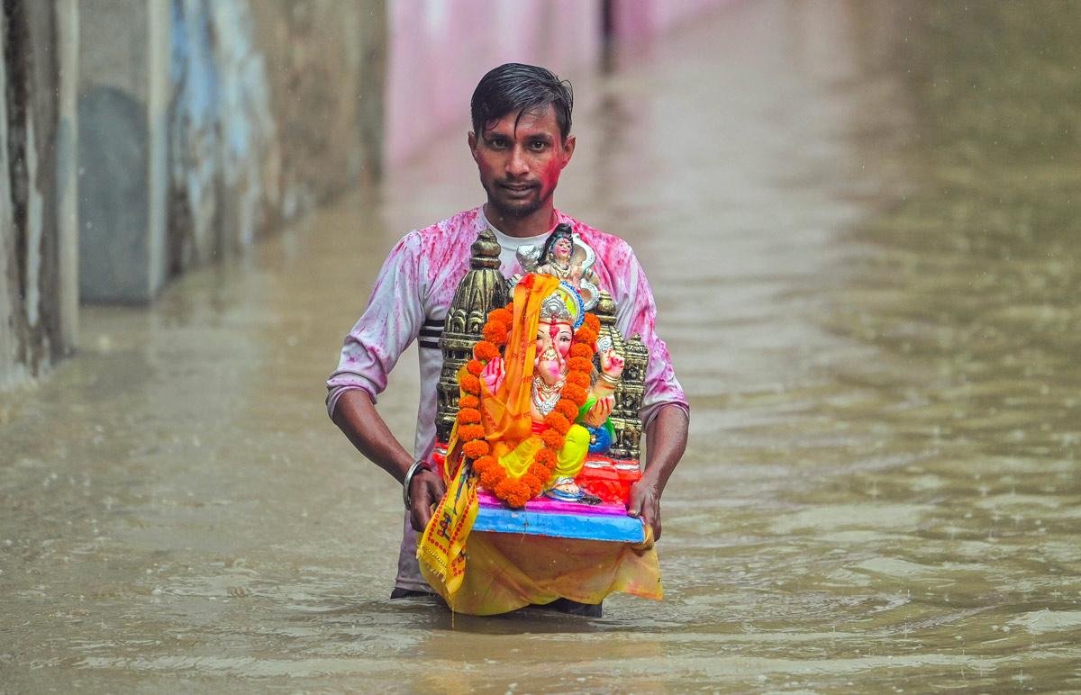 A man carrying an idol of lord Ganesh walks through a waterlogged area as the river Yamuna crosses the danger mark following incessant rainfall, at Yamuna Bazar in New Delhi