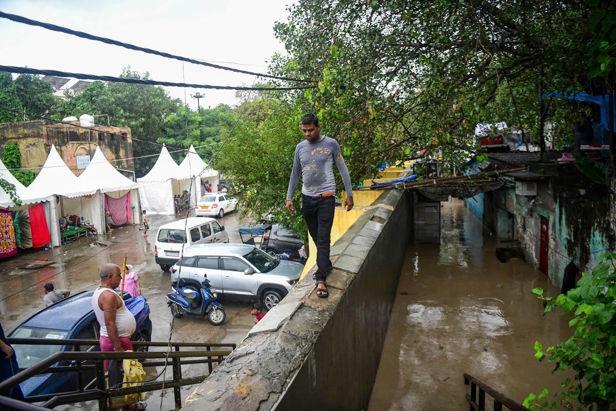 A man walks on a boundary wall of a waterlogged area as the river Yamuna crosses the danger mark following incessant rainfall, at Yamuna Bazar in New Delhi