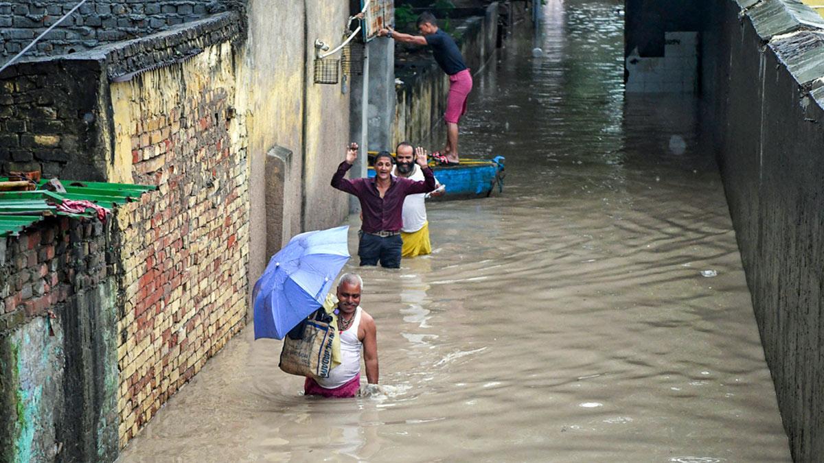 People walk through a waterlogged area as the river Yamuna crosses the danger mark following incessant rainfall, at Yamuna Bazar in New Delhi