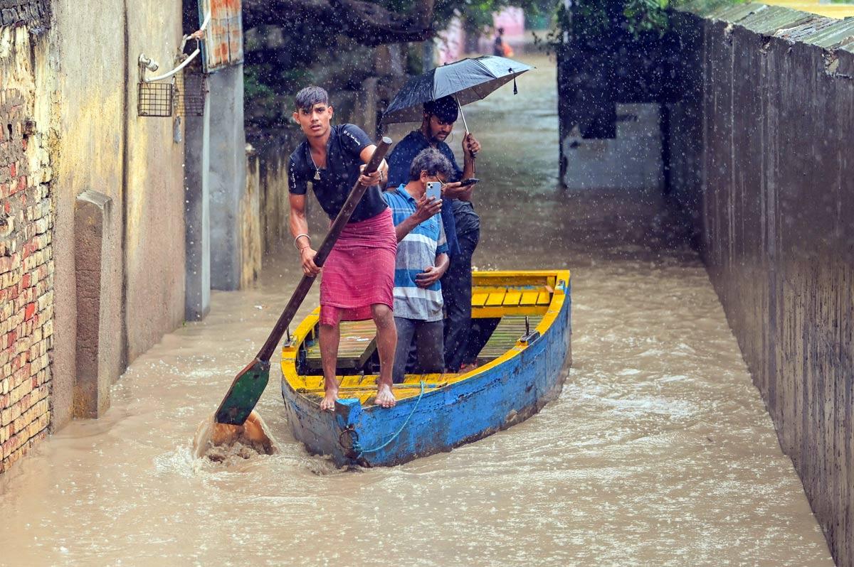 People wade through a submerged area using a boat amid rain as the river Yamuna crosses the danger mark following incessant rainfall, at Yamuna Bazar in New Delhi