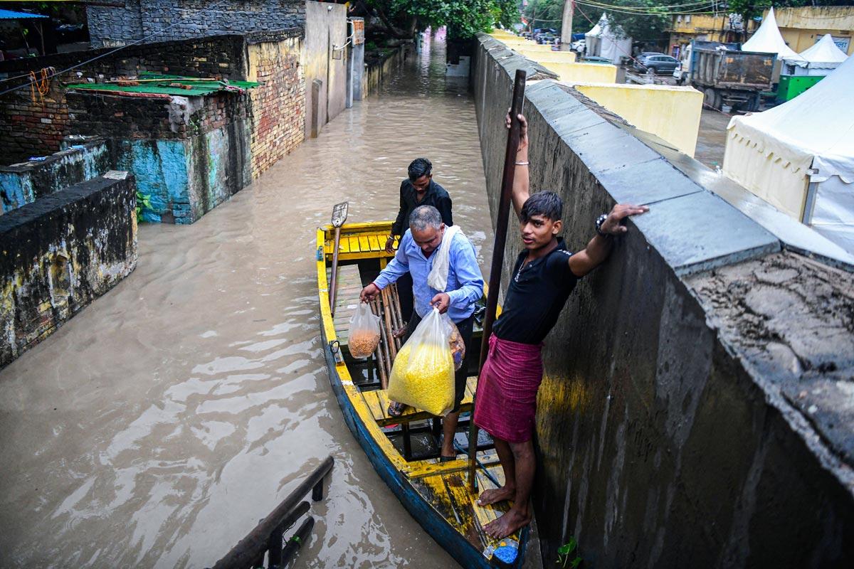 People wade through a submerged area using a boat as the river Yamuna crosses the danger mark following incessant rainfall, at Yamuna Bazar in New Delhi