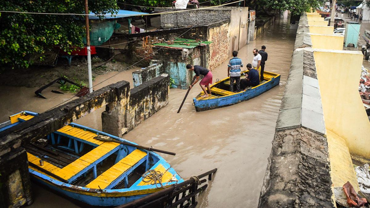 People wade through a submerged area using a boat as the river Yamuna crosses the danger mark following incessant rainfall, at Yamuna Bazar in New Delhi
