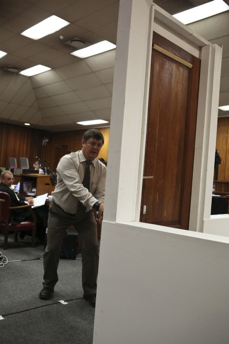 A policeman demonstrates the effect of hitting a bathroom door with a cricket bat during the trial of South African Paralympic athlete Oscar Pistorius in the North Gauteng High Court in Pretoria
