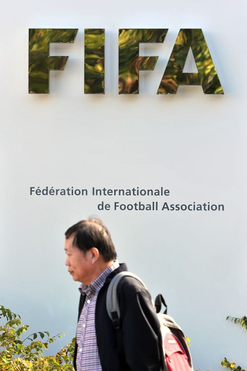 A man walks in front of the FIFA logo displayed outside the FIFA headquarters