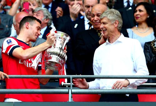 Captain Thomas Vermaelen of Arsenal passes the trophy to manager Arsene Wenger (right) after the FA Cup final against Hull City at Wembley Stadium on May 17, 2014.