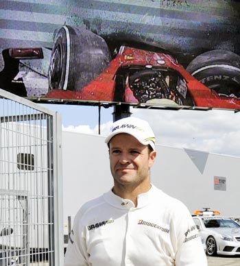 Rubens Barrichello walks past a video screen showing the Felipe Massa crash