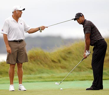 Tiger Woods hits as his caddie Steve Williams holds a club during a practice round