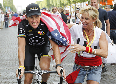 A fan drapes the US flag around Armstrong during the final parade of Tour de France on the Champs Elysees