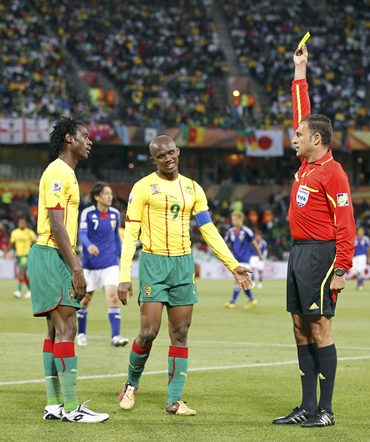Cameroon's Nicolas Nkoulou (L) receives a yellow card from referee Olegario Benquerenca (R) of Portugal as his captain Samuel Eto'o watches
