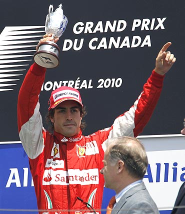 Ferrari Formula One driver Fernando Alonso holds up his third-place trophy