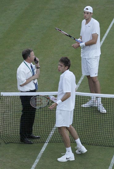 France's Nicolas Mahut and John Isner of the U.S. talk to a tournament official who suspended play due to darkness