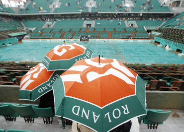 Spectators sit under umbrellas as rain interrupts play at the French Open