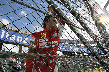 Ferrari's Felipe Massa looks out from behind a fence as his car is recovered after colliding with Force India's Vitantonio Liuzzi