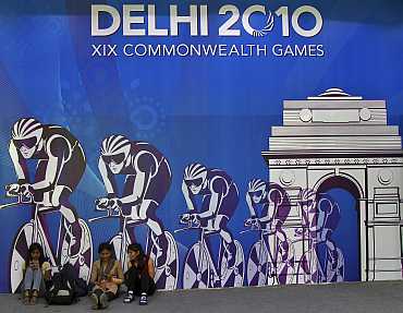 Volunteers sit in front of a board advertising the 2010 Commonwealth Games in New Delhi
