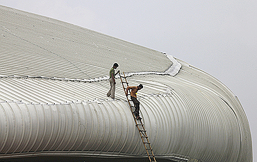 Workers climb down the roof of the weightlifting venue for the Commonwealth Games. A portion of the false ceiling at the venue caved in on Wednesday