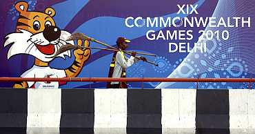 A man carries brooms in front of a board advertising the 2010 Commonwealth Games in New Delhi