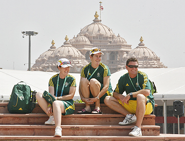 Australian athletes Lynsey Aromitage (left), Leif Selby (right) and Claire Duke sit inside the Commonwealth Games Village with the Akshardham temple in the background