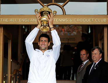 Novak Djokovic holds the championship trophy outside the members entrance at the at the All England Lawn Tennis and Croquet Club on Sunday