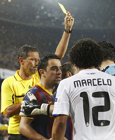Referee Frank de Bleeckere shows the yellow card to Real Madrid's Marcelo (right) even as he argues with Barcelona's Xavi (centre)