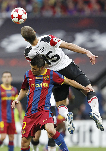 Manchester United's Nemanja Vidic (top) jumps for the ball over Barcelona's David Villa