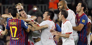 Cesc Fabregas is grabbed by the throat (left) as Barcelona and Sevilla players argue after a penalty during their La Liga match at Camp Nou stadium in Barcelona on Saturday