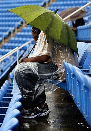 A fan sits down with umbrella as rain falls to delay matches on Tuesday