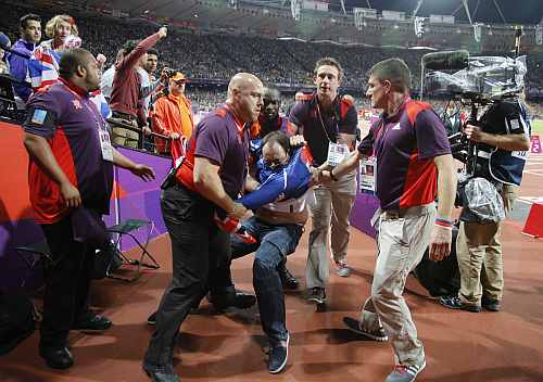 A spectator is detained by security after a beer bottle was thrown on to the track during the start of the men's 100 metres final