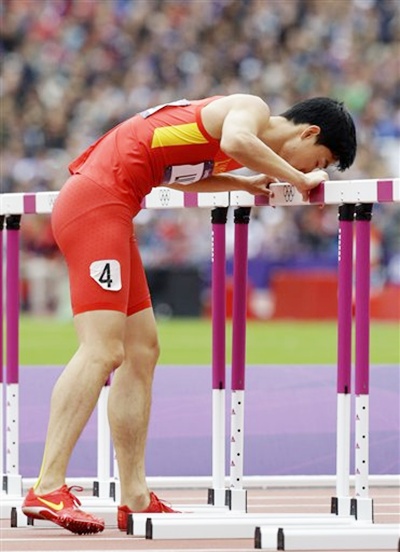 China's Liu Xiang kisses a hurdle as he hops to the finish line after he failed to clear a hurdle and injured himself