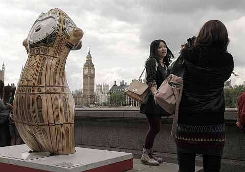 A tourist is photographed in front of Big Ben near an Olympic mascot painted in the likeness of Big Ben