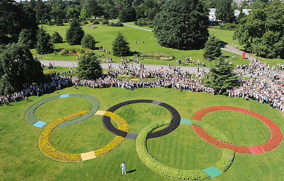 Torchbearer Oliver Golding holds the Olympic Flame in between the Olympic Rings at Kew Gardens