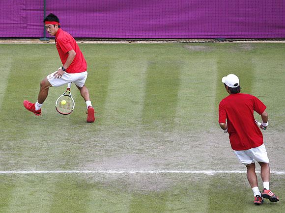 Japan's Go Soeda watches as Kei Nishikori hits a return through the legs against Switzerland's Roger Federer and Stanislas Wawrinka