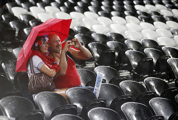 Fans shelter themselves with an umbrella as rain stops play
