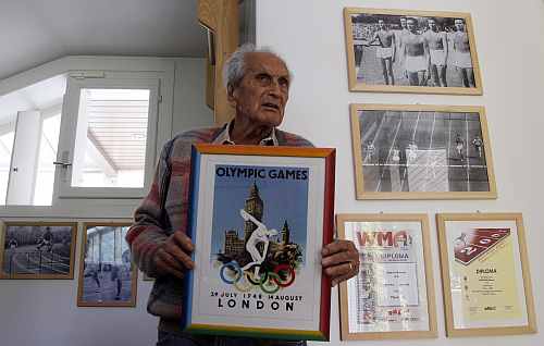 Ottavio Missoni holds a framed poster for the 1948 Olympics in London at his house in Sumirago