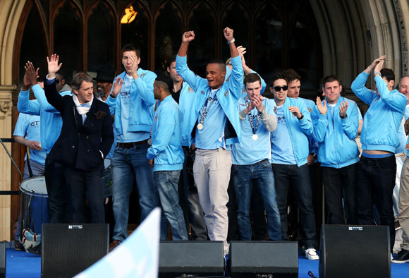 The players of Manchester City wave to their supporters outside Manchester Town Hall as they leave for the start of their victory parade around the streets of Manchester on May 14